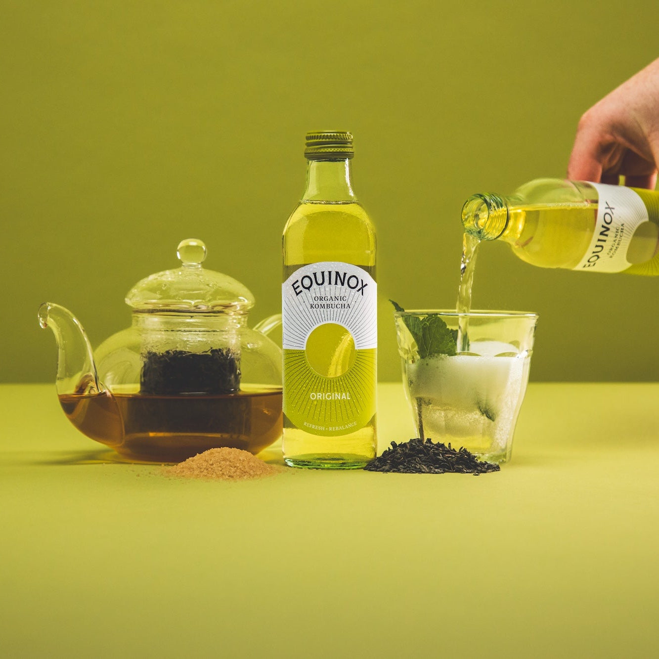 Person pouring a bottle of Equinox juice into a glass with a green background