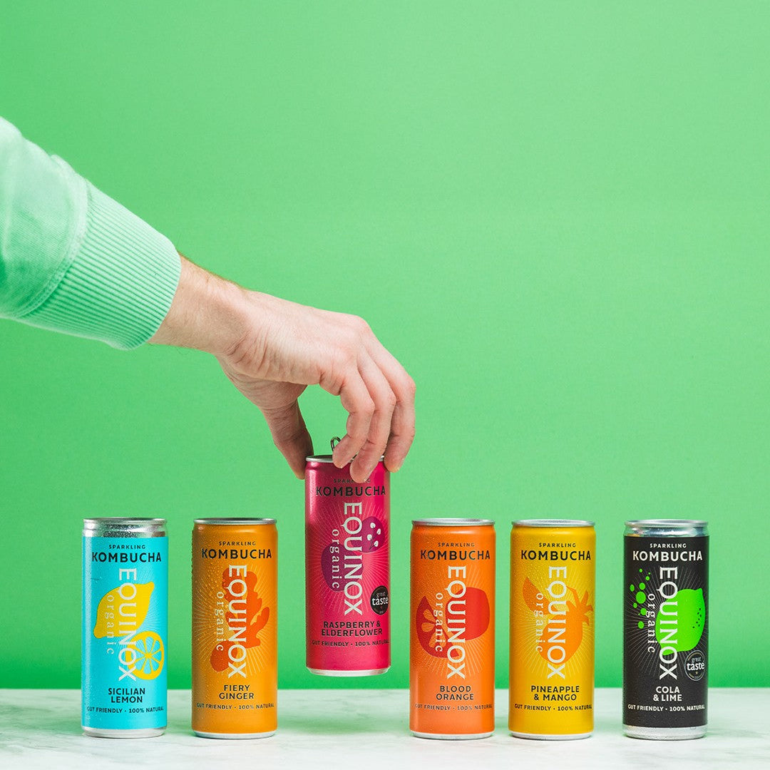 Hand picking a can of EQUINOX Kombucha against a green background